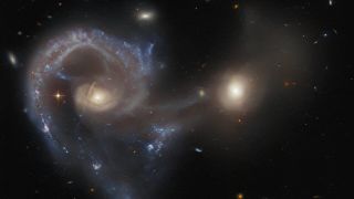 a long spiral galaxy is near another, less gaseous galaxy or supermassive blackhole