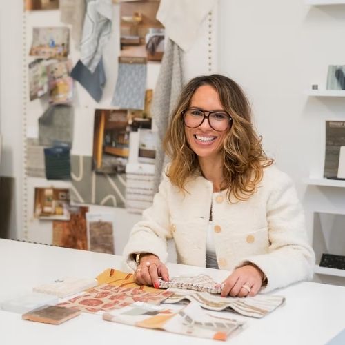 Image of a woman in a white jacket sitting in a white office room with fabric samples around her.