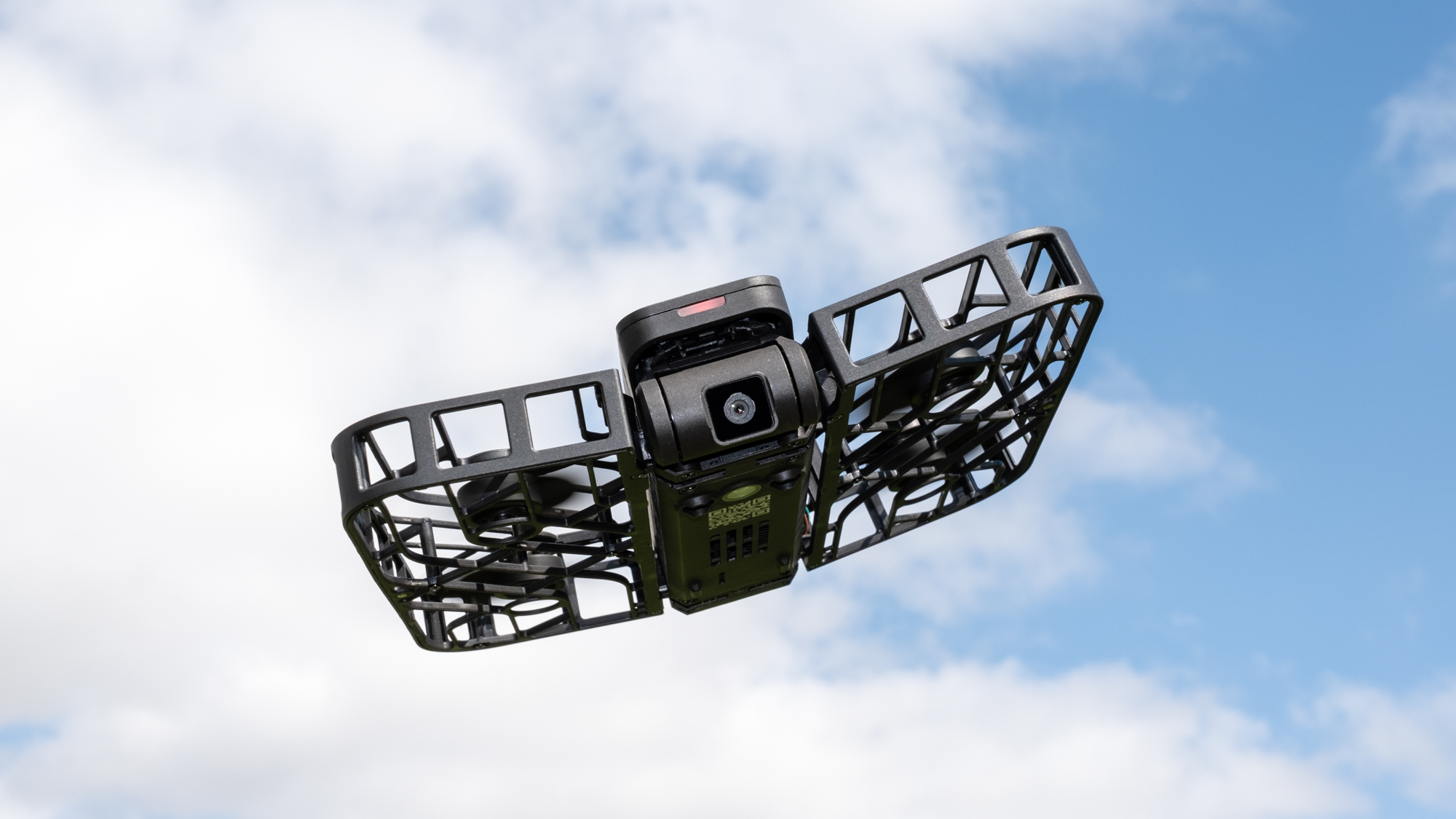 HoverAir X1 flying against a blue sky with white clouds