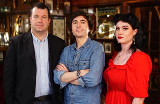 Dr Ciaran O'Keefe, Danny Robins and Evelyn Hollow stand in a row in a bar, facing the camera