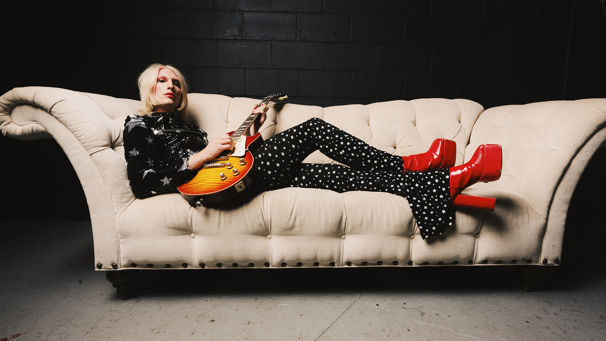 A photo of Alice Cooper band guitarist Gyasi Heus laying on a sofa playing a Gibson Les Paul