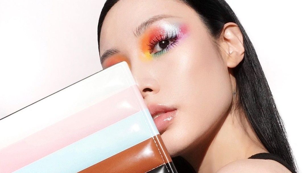 A woman with a rainbow eye makeup look holding a makeup palette.