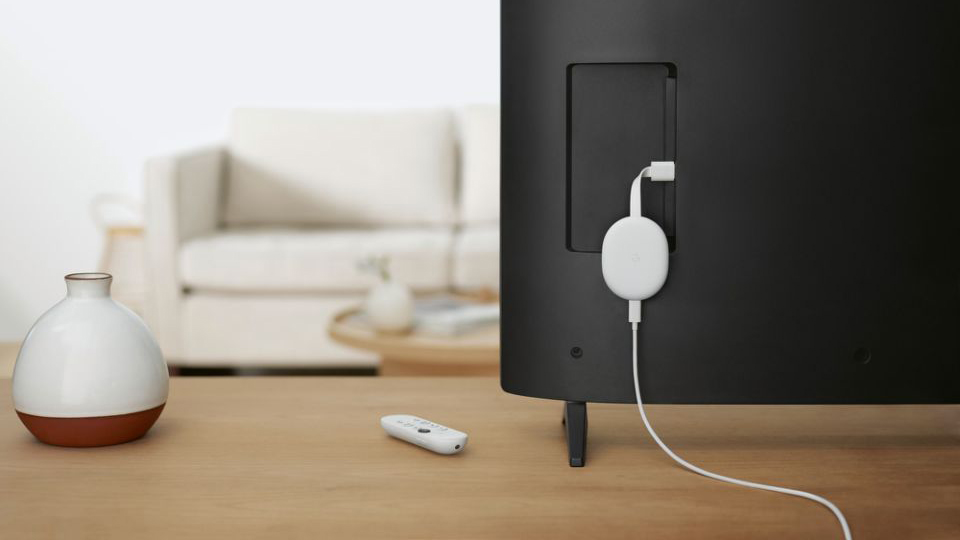 En TV med Google Chromecast-dongle på baksiden i en stue med en sofa i bakgrunnen.