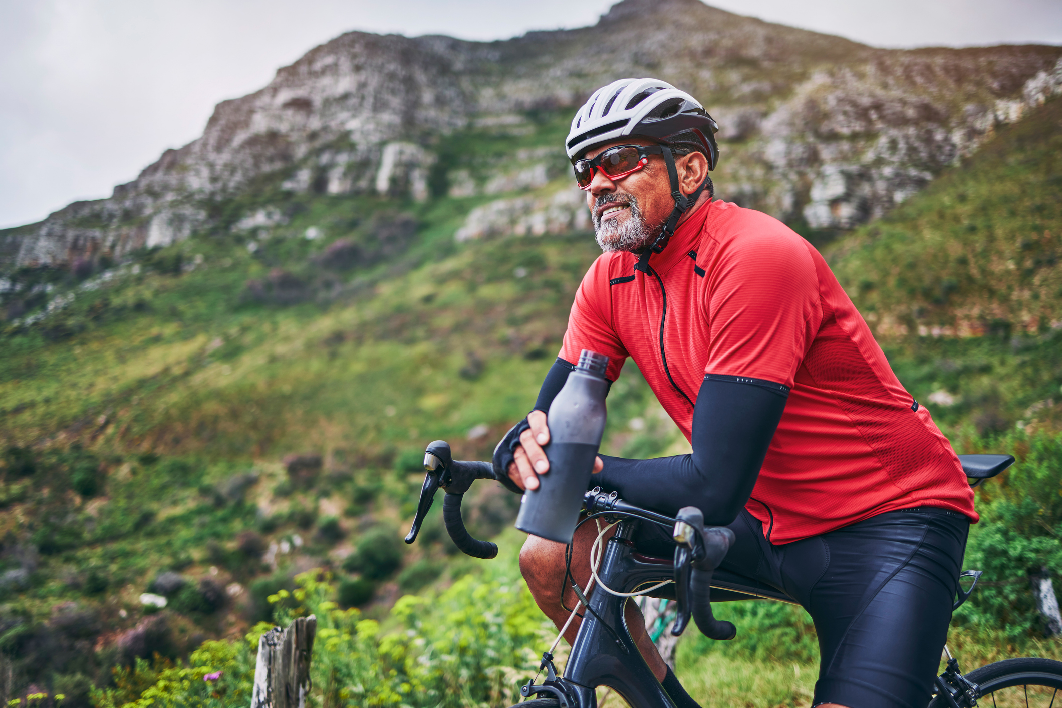 Fitness, cycling and water with man on bike in nature for sports, training and challenge. Exercise, workout and health with mature person on bicycle in mountains for energy, freedom and performance