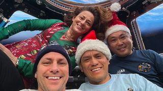 four astronauts in front of space station windows wearing santa hats or holiday clothing