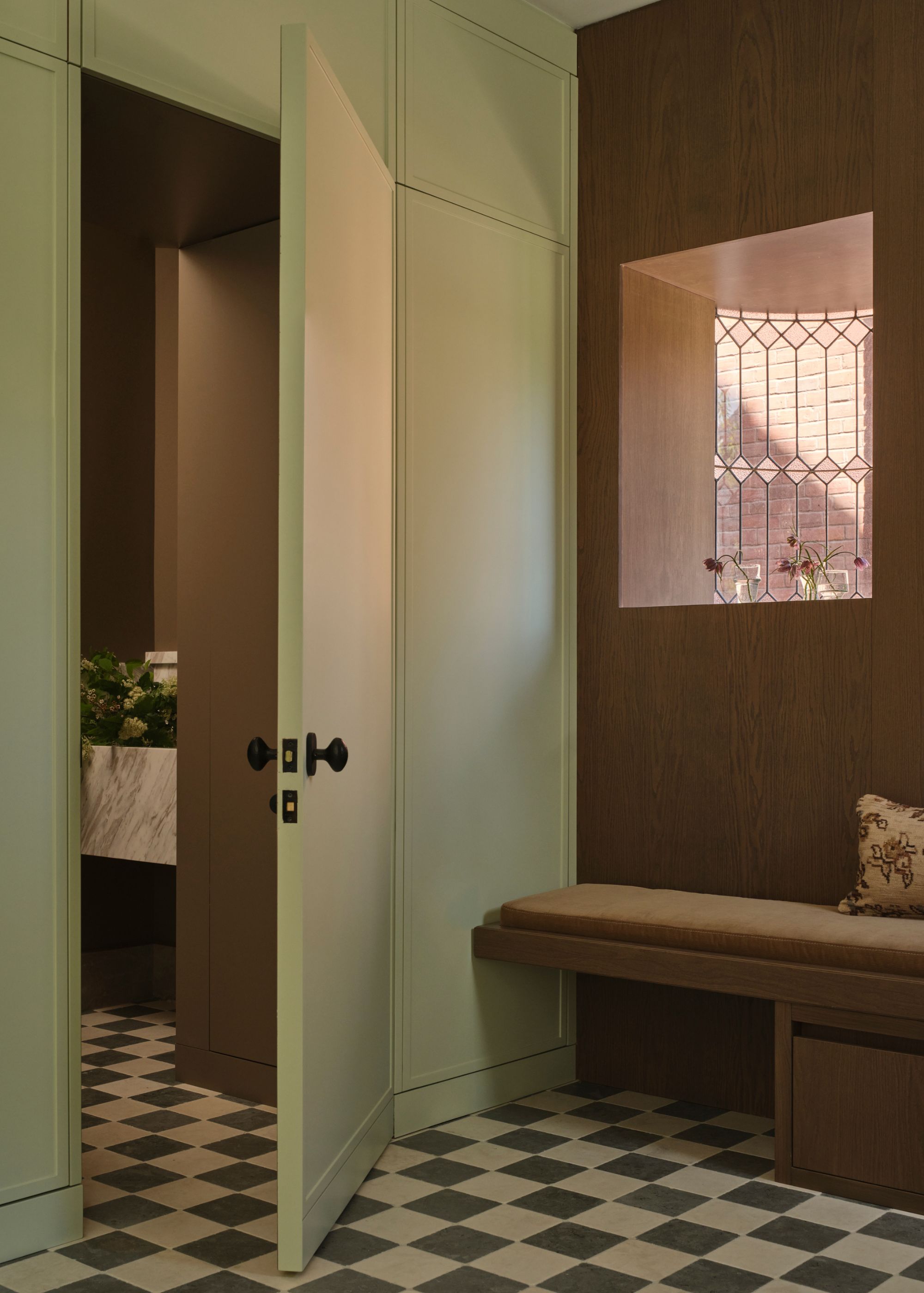 A sage green door, checkerboard flooring, a brown bench, and storage spots