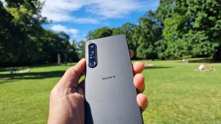 Sony Xperia 1 IV holdt i hånden med bagsiden synlig. I baggrunden er der park og mennesker på græsset.