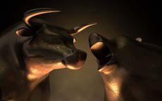 An abstract closeup of two gold cast statuettes depicting a stylized bull and a bear in dramatic contrasting light representing a financial market trends on an isolated dark background