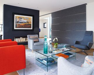 A dark blue, white and red apartment living room scheme with armchairs facing each other around an acrylic coffee table.