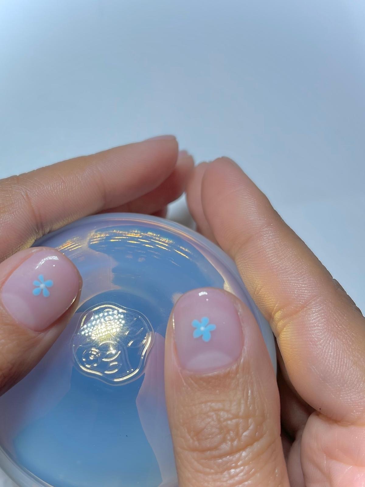A very close-up photo of Harriet Westmorelands milky floral nail art, featuring a sheer milky manicure and a small blue flower on each thumbnail
