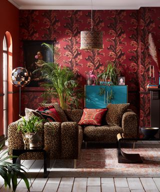 A maximalist living room corner idea with leopard print sofa, red wallpaper decor and wall art