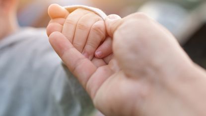 A newborn holds an adult's fingers.