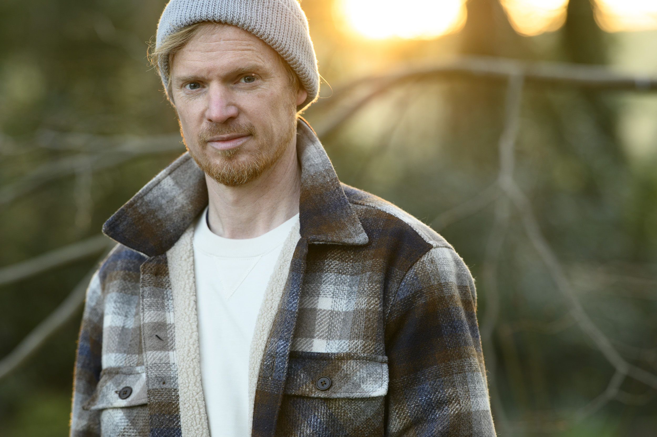 Portraits of a man in a beanie hat and shacket and golden hour with dappled light in background