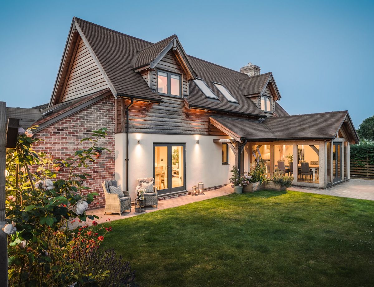 An oak frame home with timber cladding and exposed red brick, surrounded by a green lawn