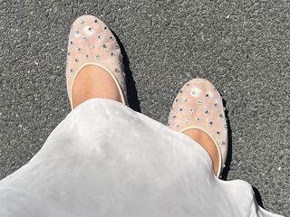 Ana wears white skirt and white mesh flats with rhinestones on them.