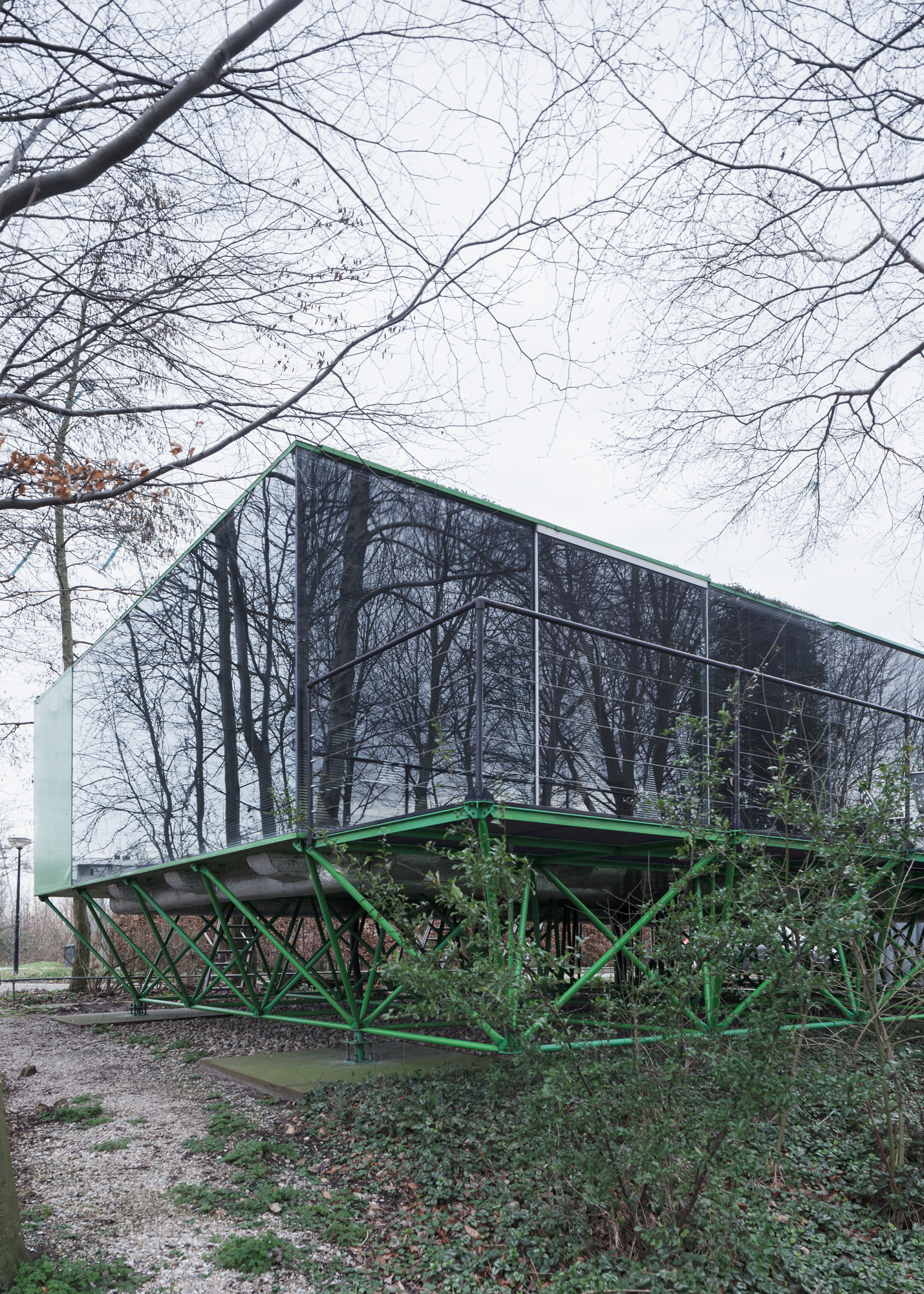 view of a corner of the house. the glass walls reflect the bare trees around