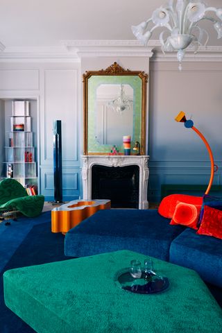 A living room with a teal ottoman and chair, paired with red pillows