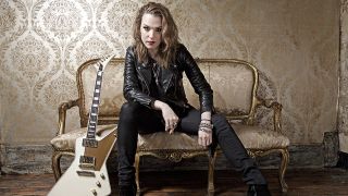A promotional photograph of Lzzy Hale sat with a guitar
