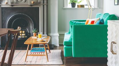 A living room with a bright green sofa and a mid-century modern style coffee table on a striped rug in front of a fireplace