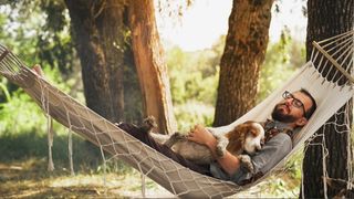 A man and a dog sleeping in hammock in forest