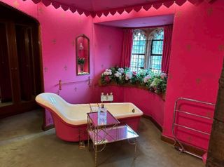 A pink bathroom with pink bath and table next to the bath