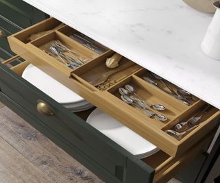 A pull out utensil drawer inside a larger kitchen storage drawer, painted dark green with gold hard wear