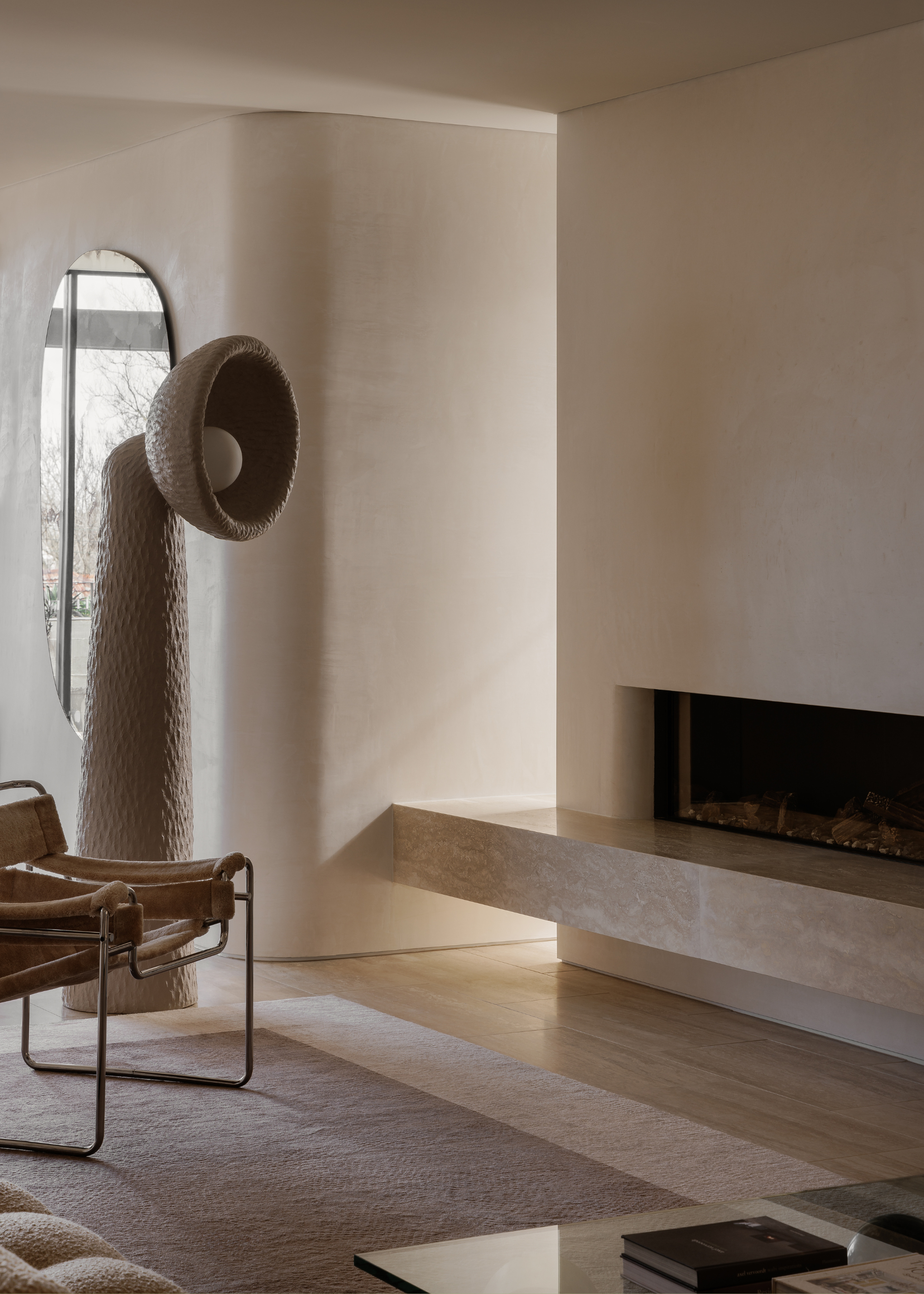 A minimalist living room with a tall floor lamp, a metal chair and a marble fireplace with a ledge