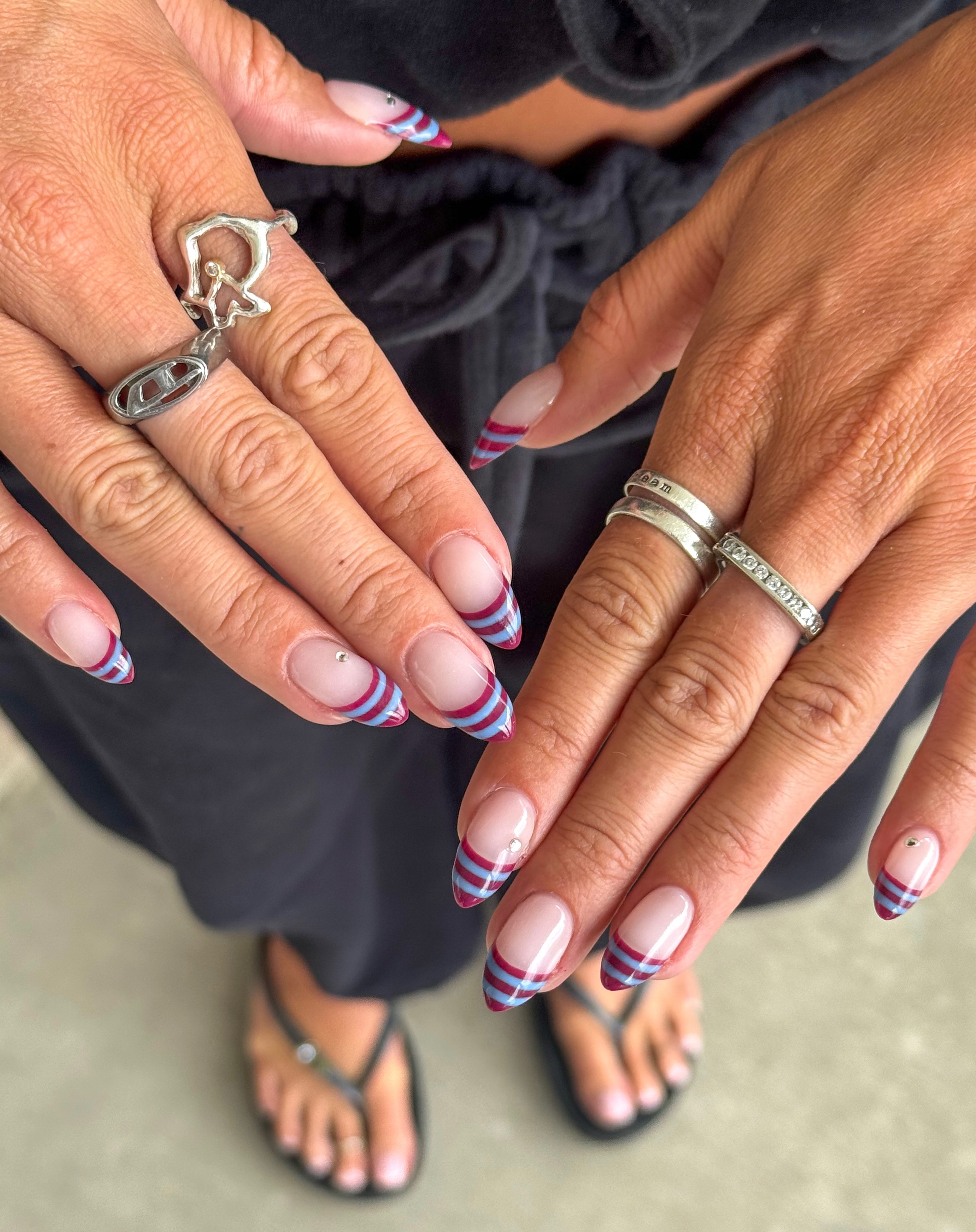 Sheer almond nails with layered burgundy and baby blue curved stripes along the tips