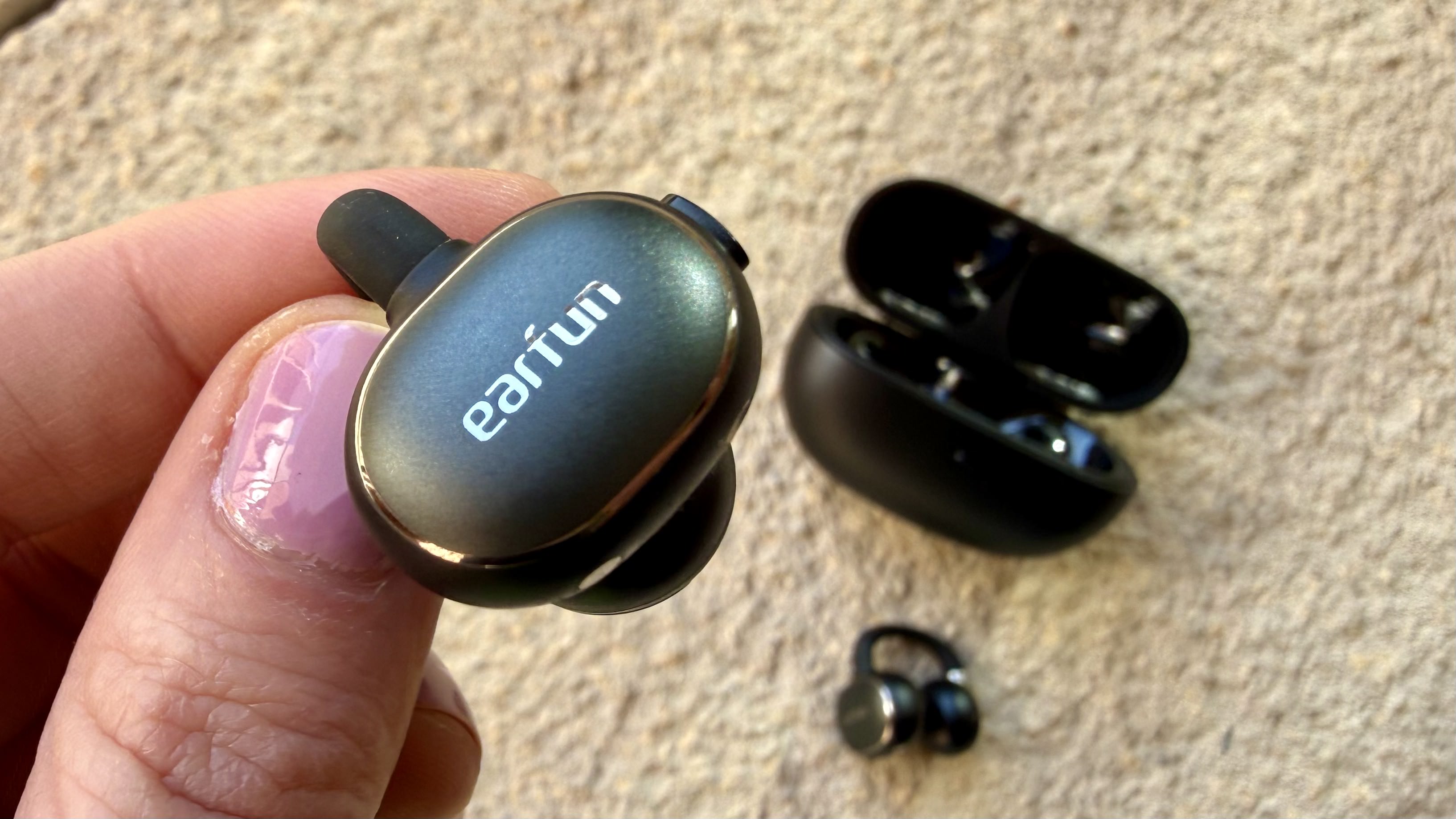 Someone holding one of the Earfun Clip 2 earbuds above the charging case