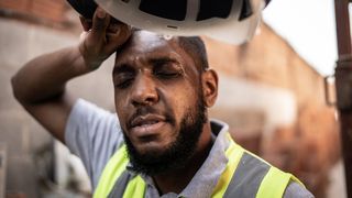 A male construction worker wipes sweat off his forehead.