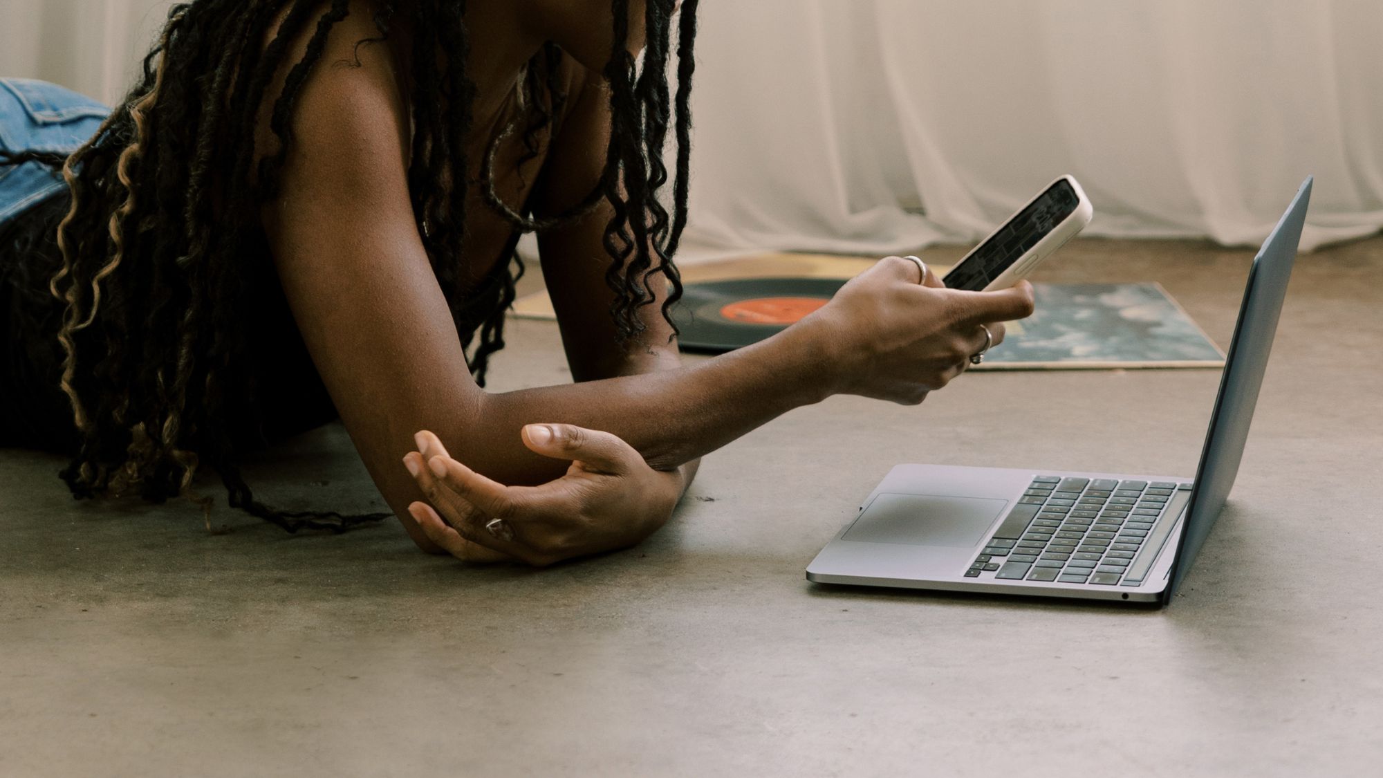 A woman scrolling on her phone, working on her laptop on the floor
