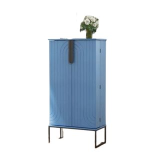 A rectangular cornflower blue kitchen cabinet with black iron legs, black handles, and a small vase of white flowers on top of it