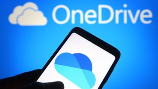 The Microsoft OneDrive logo on a smartphone in front of the service's branding on a blue wall