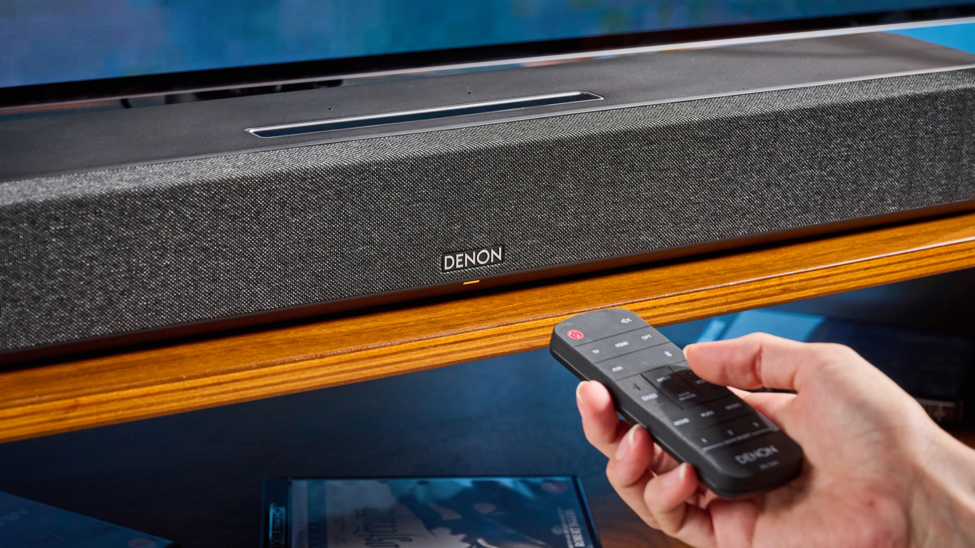 the denon home sound bar 550 with a gray mesh casing and touch controls for bluetooth on the top with a remote and smart home integration