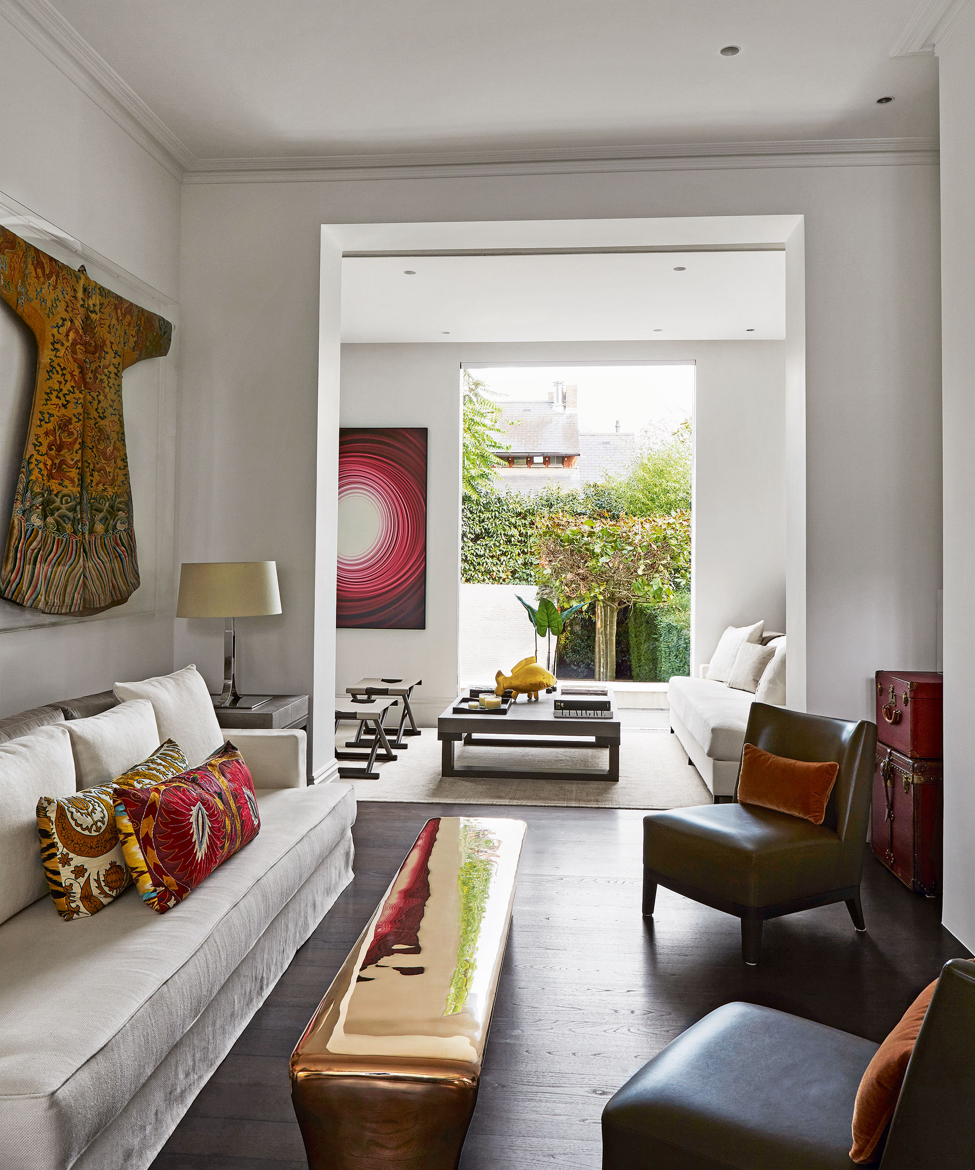 An open plan living room with white walls and wooden floors with a large window looking out into a back garden.