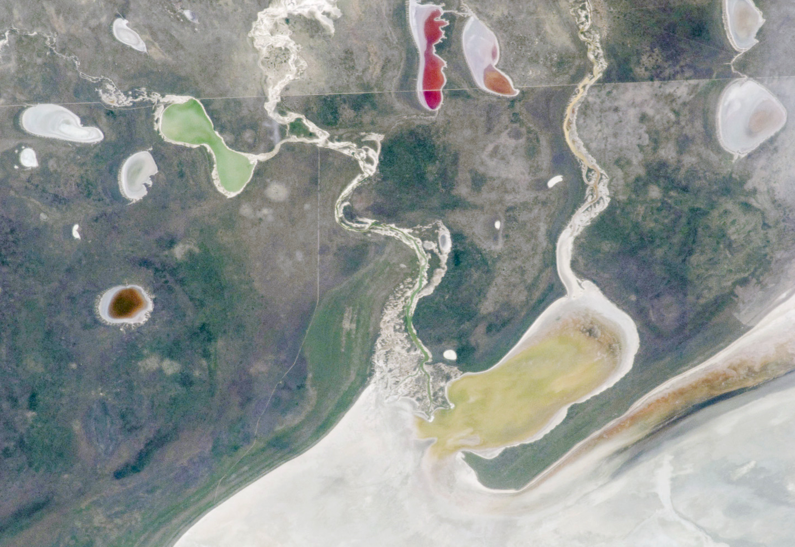 A satellite photo showing a pair of rivers and a series of colorful lakes surrounding a giant white expanse