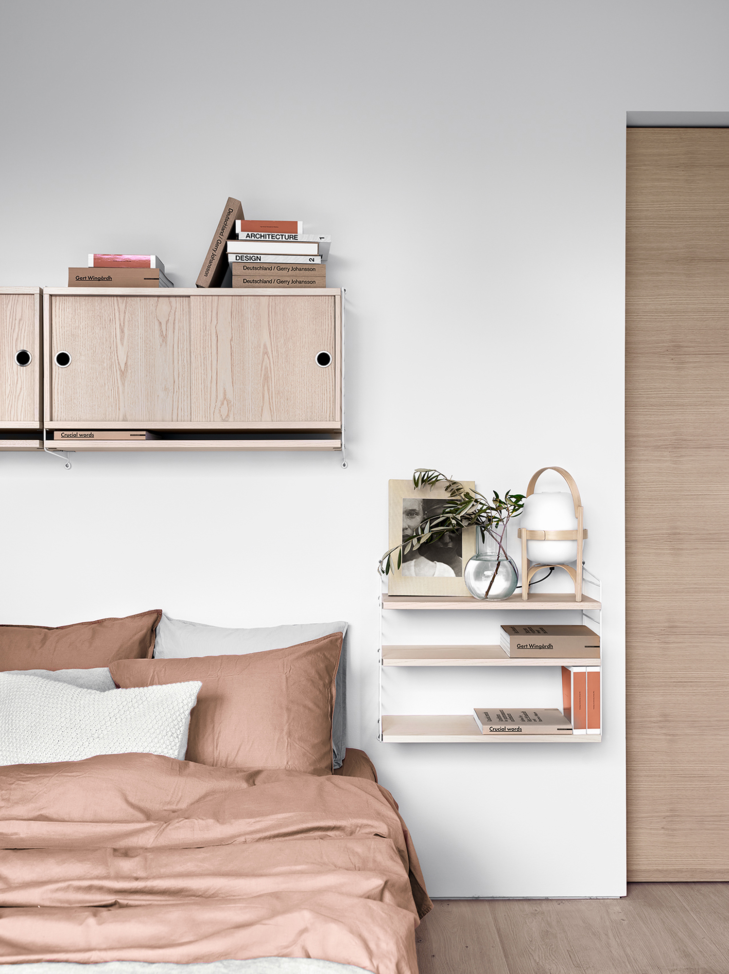 White bedroom with mounted sliding shelving and floating shelf side table unit next to bed dressed with rust and cream bedding