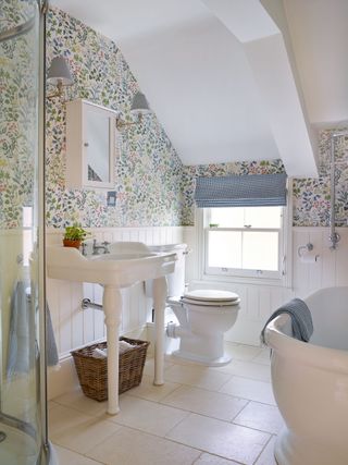 bathroom with floral wallpaper white tongue and groove paneling shower and white freestanding bath and vintage style wall lights with gingham shades