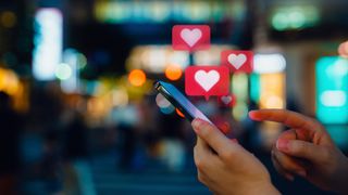 edited photo shows a woman's hands as she lifts a finger to swipe on a phone. Hearts in speech bubbles are shown popping up above the phone, indicating likes or notifications