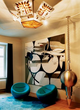 The living room at von Habsburg’s apartment features Crashedcaradjust, 2001, by Stefan Hirsig, on the wall; Untitled (Pen del 3), 2002, by Sylvie Fleury, hangs from the ceiling; the chairs are 1970s and the lampshade is from a Viennese junk shop. Photography: Philip Sinden
