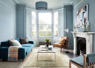 blue living room with walls and woodwork painted one color, wooden floor, rug, blue couch, coffee table, leather armchair, fireplace, artwork