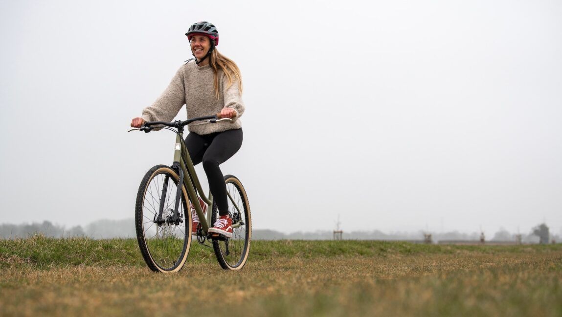 A woman rides an olive hybrid bike through a field