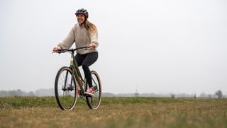 A woman rides an olive hybrid bike through a field