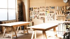 An empty DIY workshop with an organized pegboard wall of tools and two empty workman desks