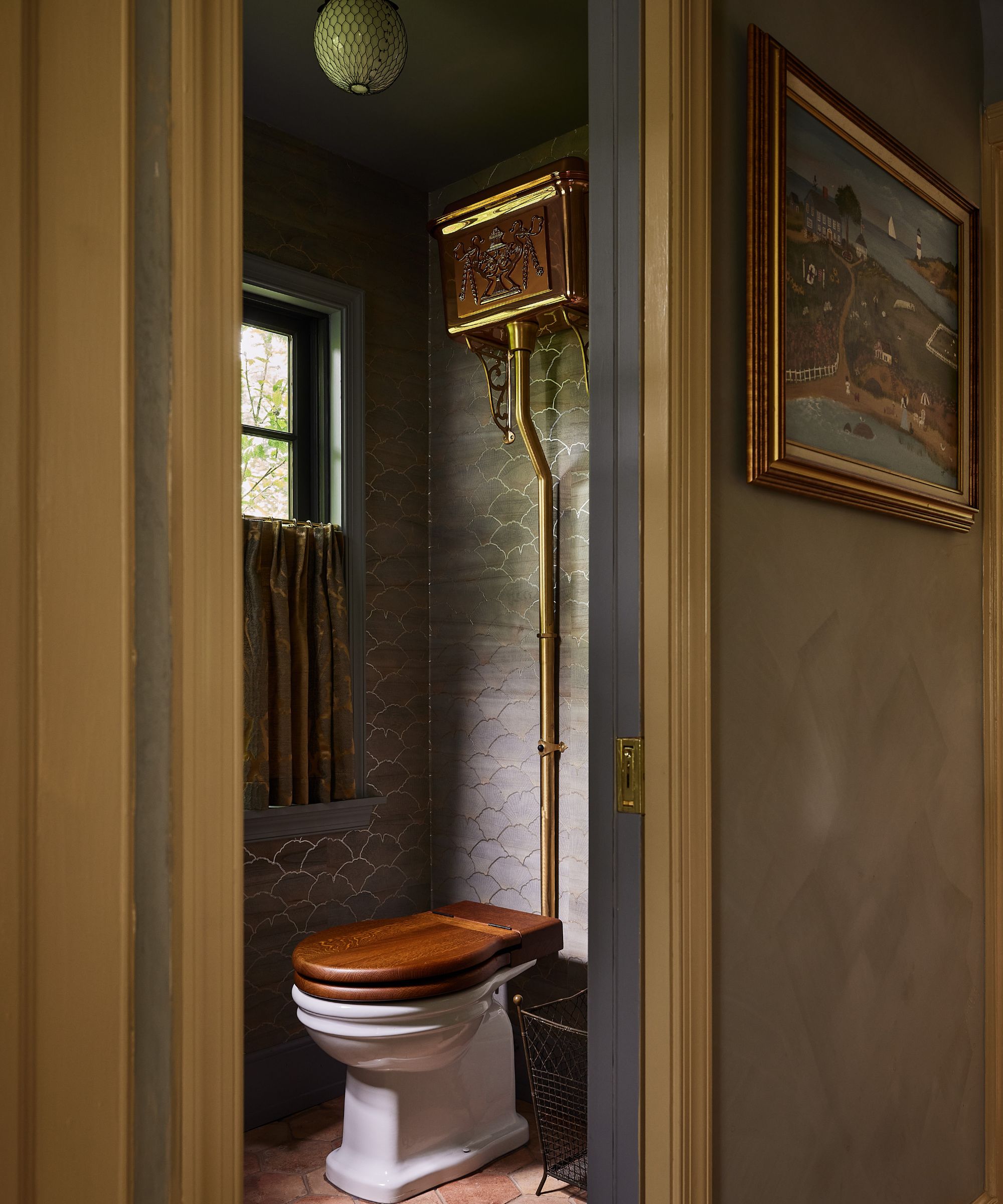 a small powder room with fish scale style dark blue wallpaper, a copper high cistern toilet, terracotta floor, and a cafe curtain at the window