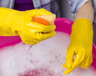 person wearing yellow rubber gloves and holding a sponge over a bucket of soapy water