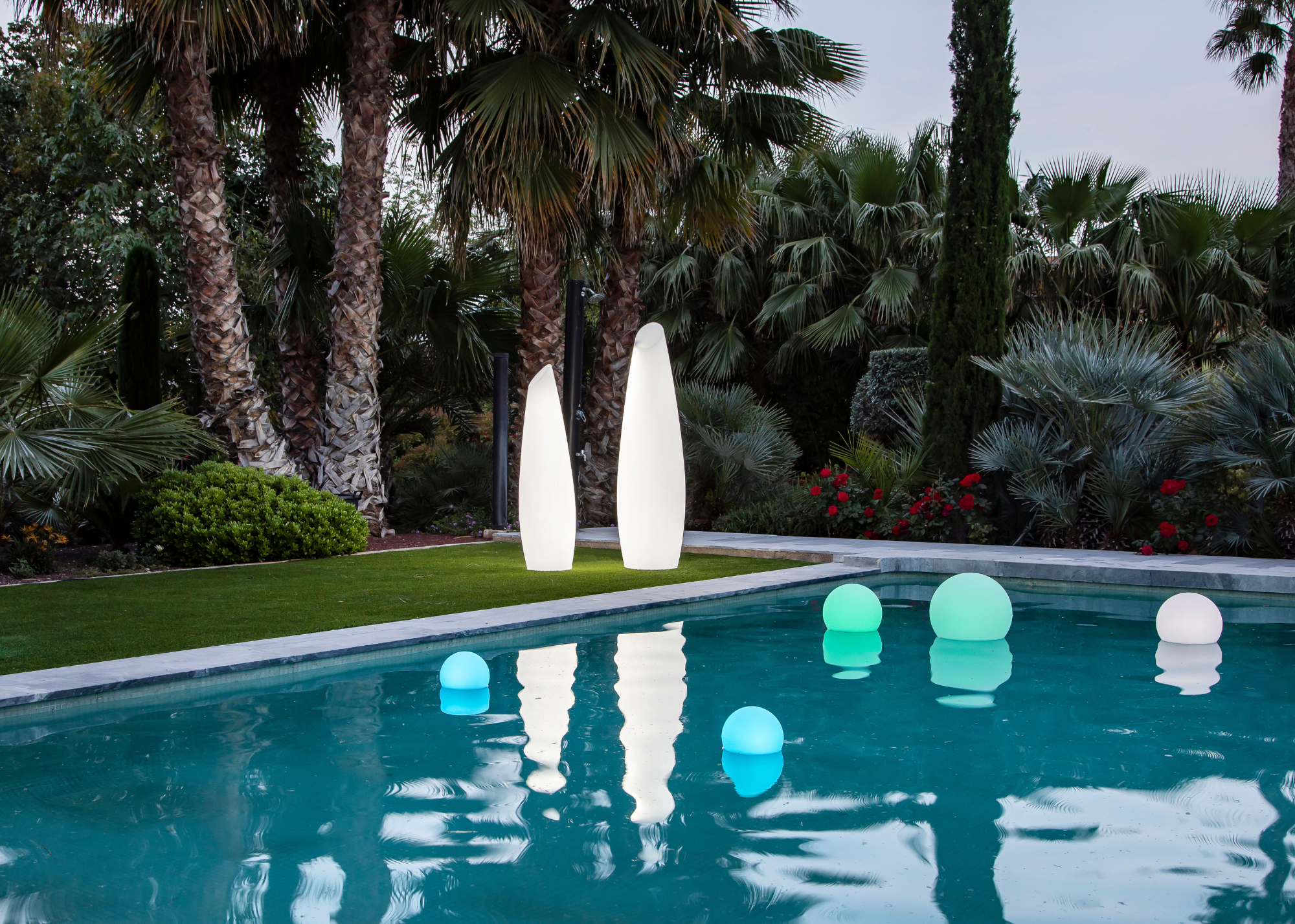 A set of two structured floor lamps on a lawn beside a pool with floating spherical lamps