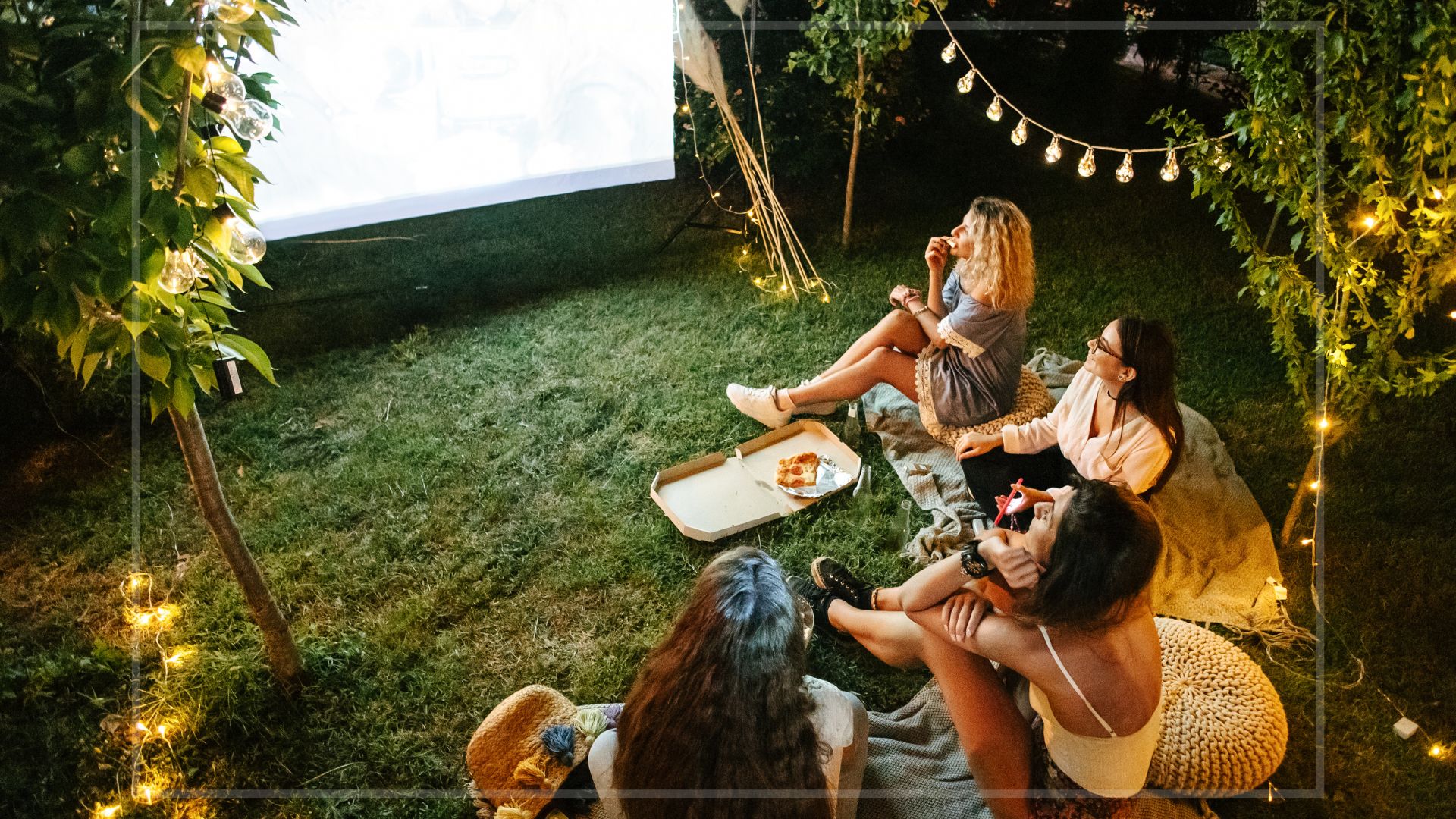 Friends watching a film on a projector outside in the garden