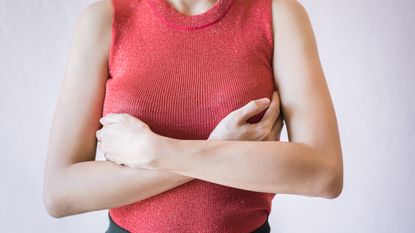 midsection of woman checking breasts wearing red jumper 