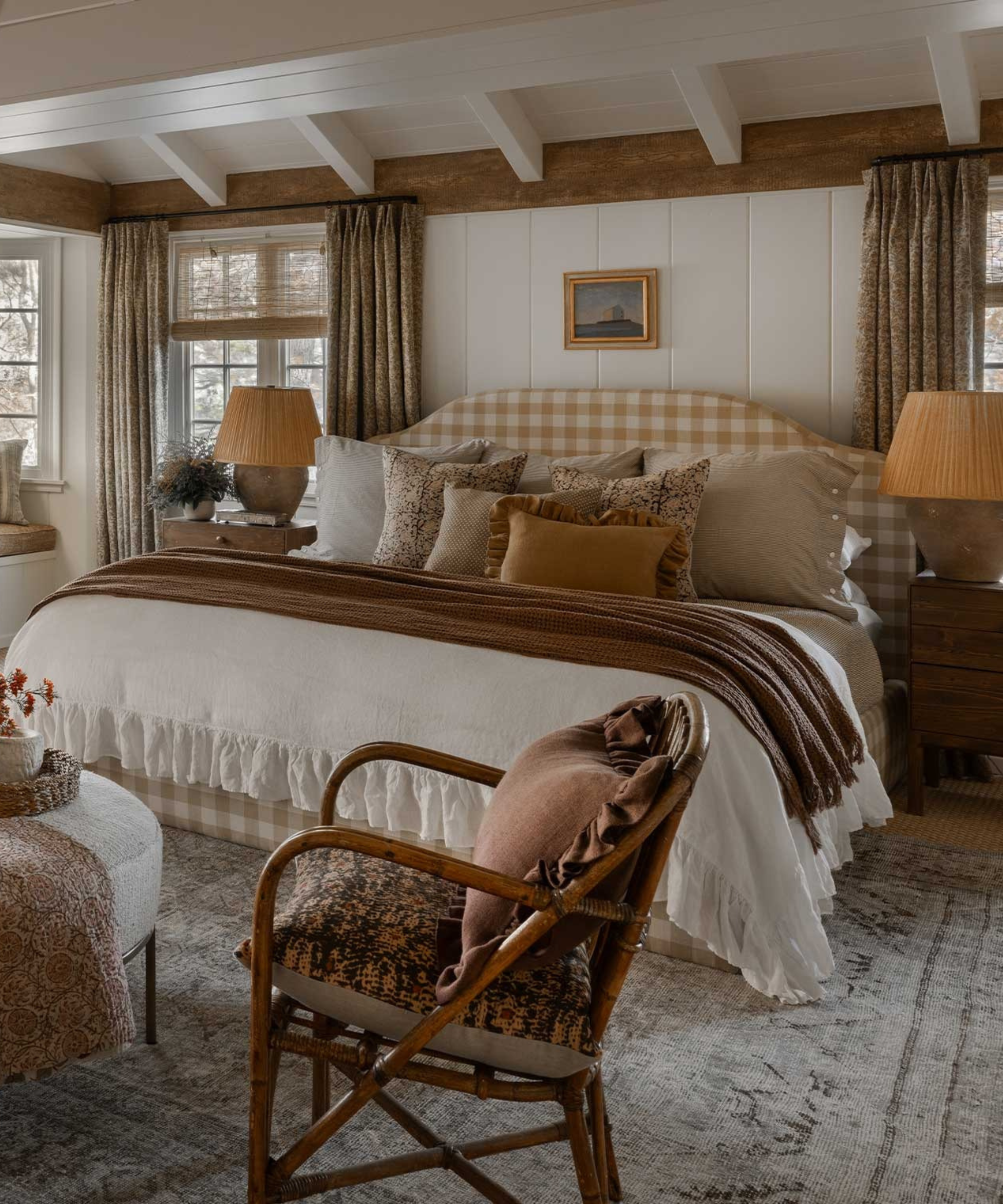 a cottage core bedroom with a bed with many pillows on top, a wooden accent chair, symmetrical side tables, and exposed beams on the ceiling